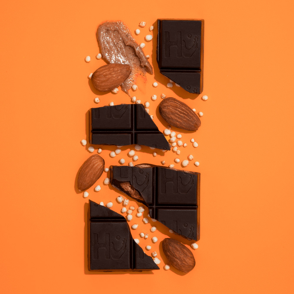 A broken Hu chocolate bar on an orange background with puffed quinoa and almonds