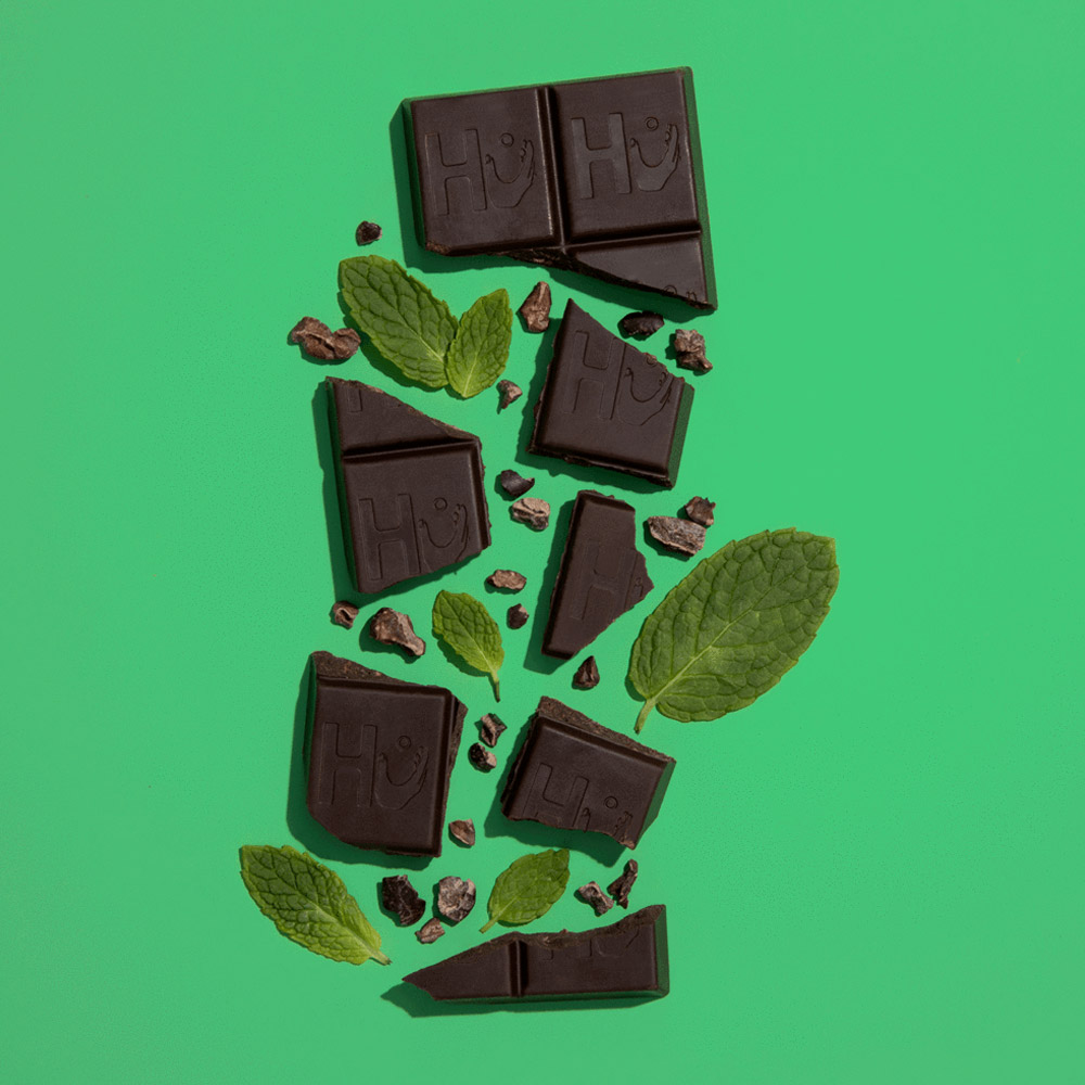 A broken Hu chocolate bar next to mint leaves and cocoa nibs