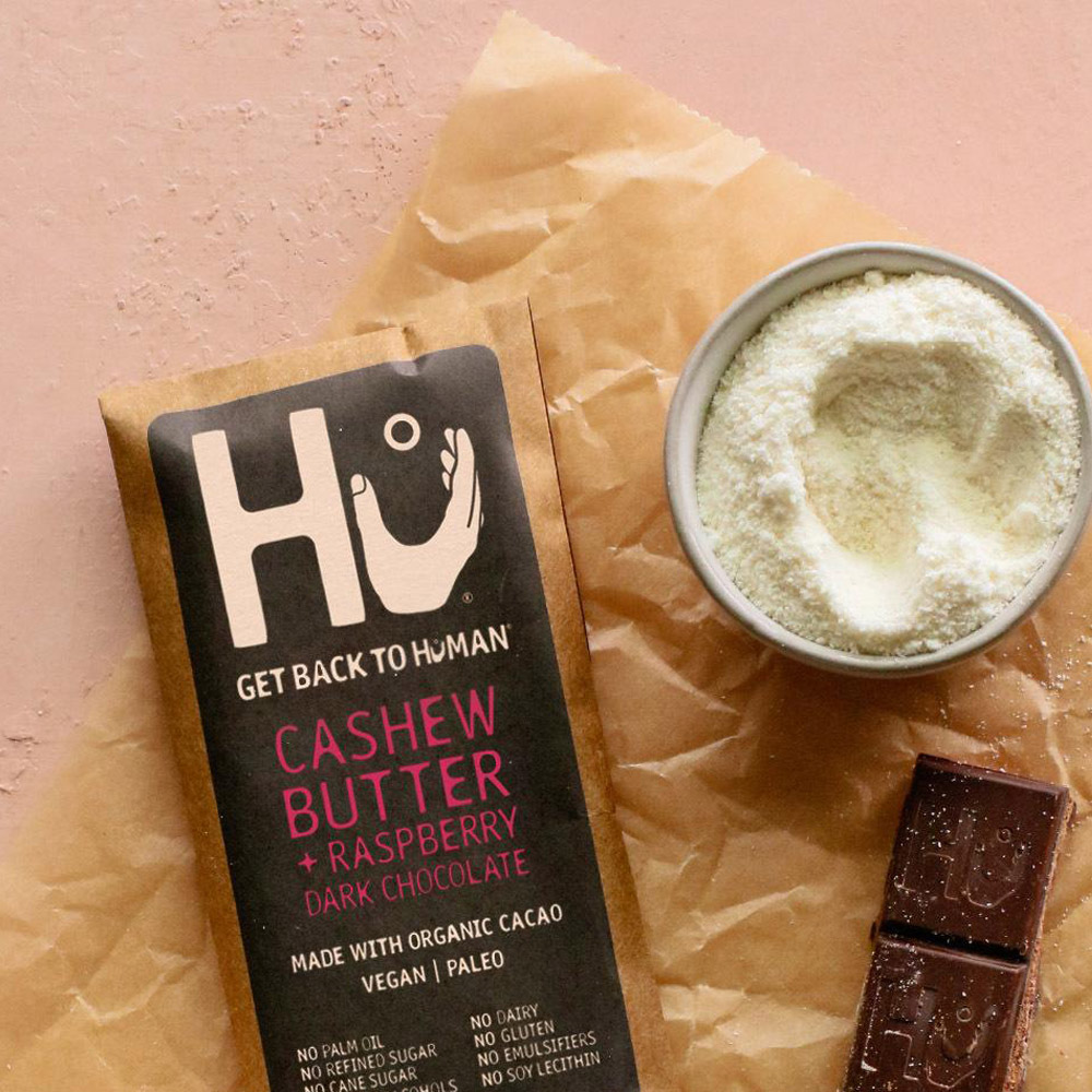 A Hu Cashew Butter and Raspberry Jelly Organic Dark Chocolate Bar next to a bowl of almond flour and two pieces of chocolate