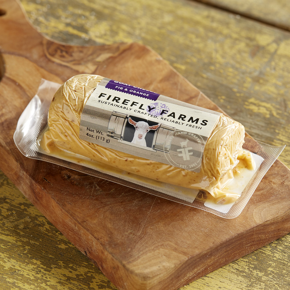 A log of Firefly Farms Fig & Orange fresh goat cheese in its packaging on a wood board