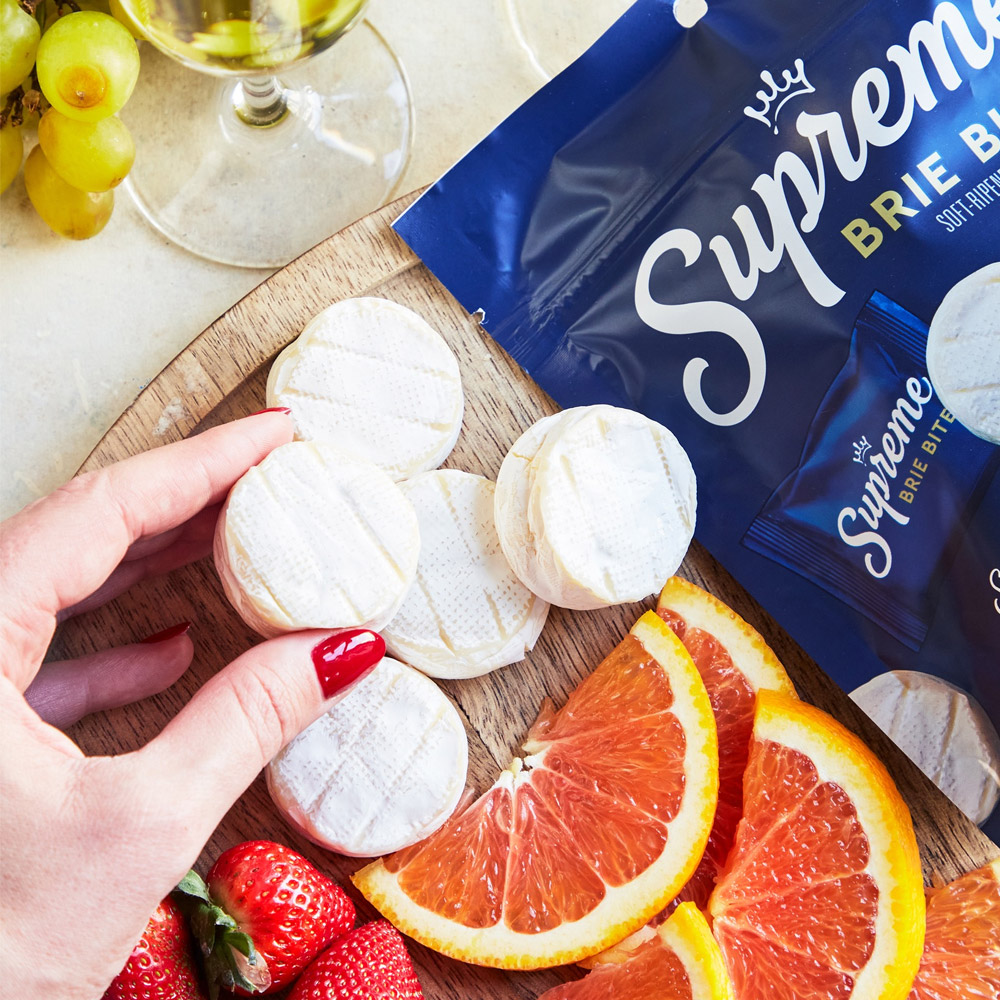 Unwrapped Supreme Brie Bites on a wood board next to the bag and orange slices