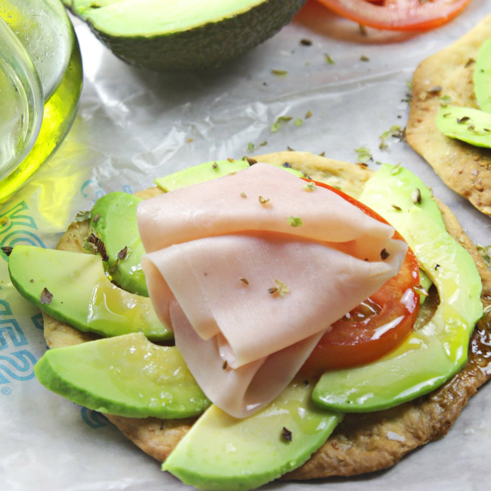 A torta topped with avocado and tomato and ham