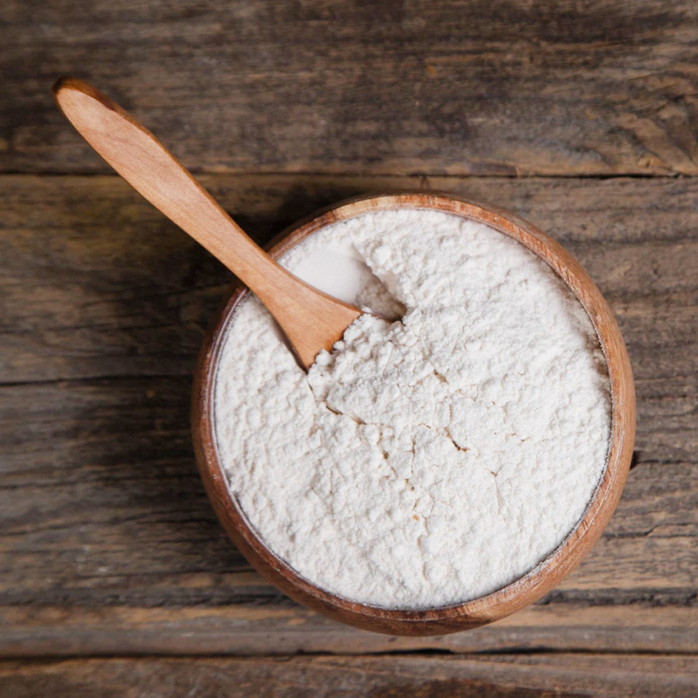A bowl of flour with a wooden spoon on a wood background
