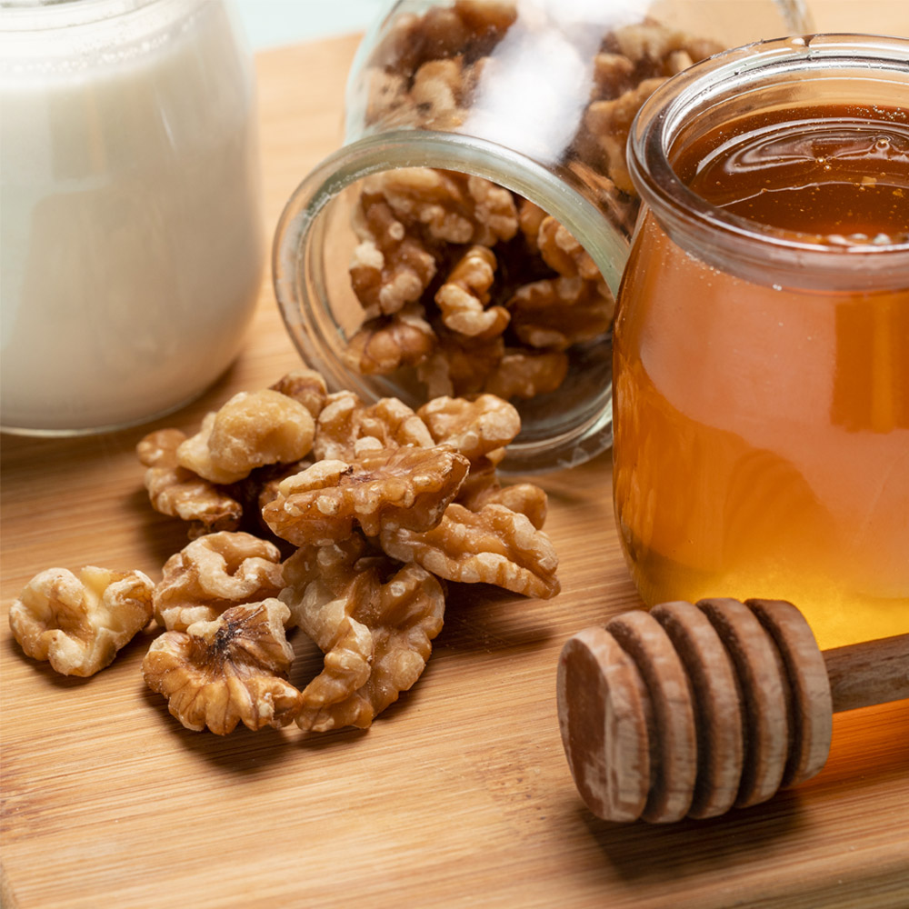 A jar of honey next to a spilled jar of walnuts