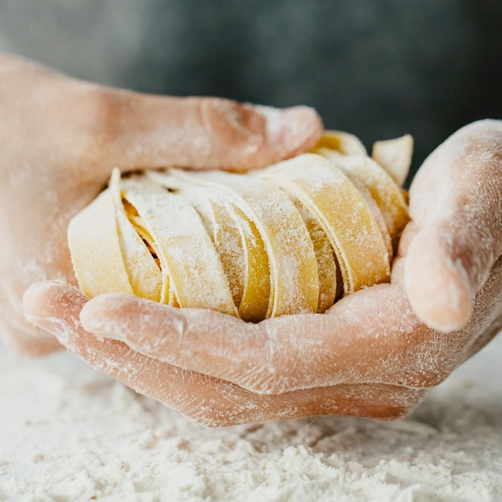 Floured hands holding long cuts of pasta over a pile of flour