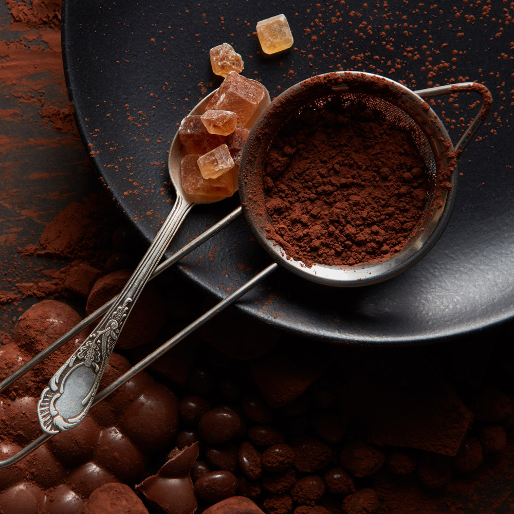 Cocoa powder in a sieve on a black plate