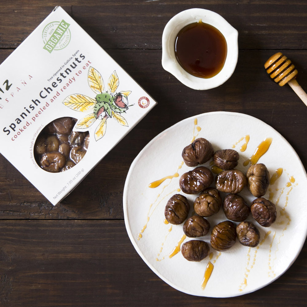 A box of Matiz Organic Chestnuts laying next to a plate of chestnuts and a bowl of honey