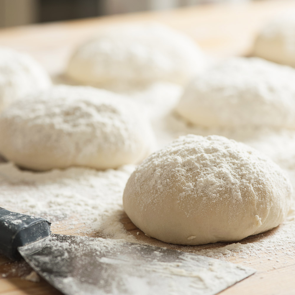 Spriana pizza dough balls on a counter with flour