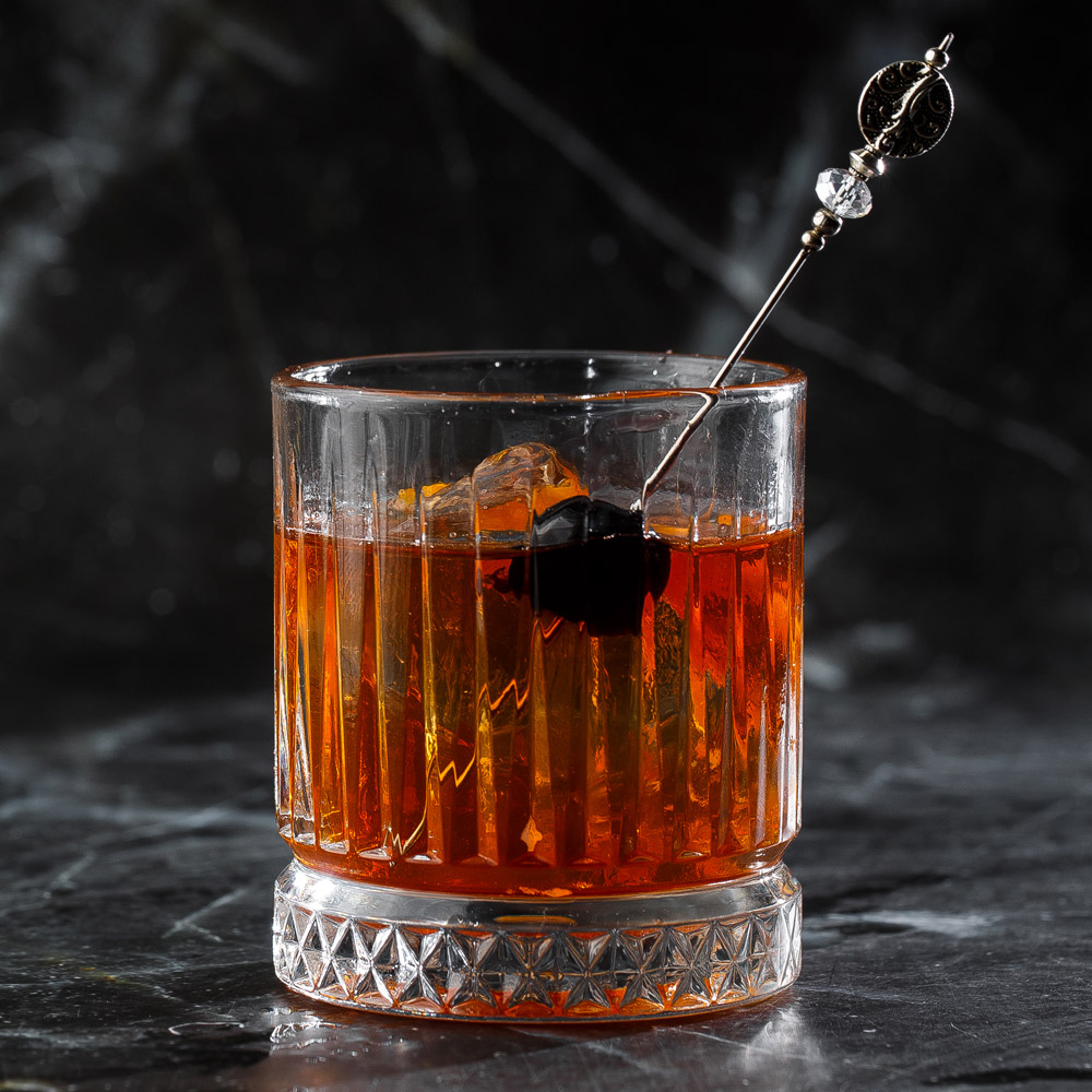 Old fashioned cocktail consisting of bourbon angostura bitter sugar cubes a few drops of water ice cubes orange maraschino cherry