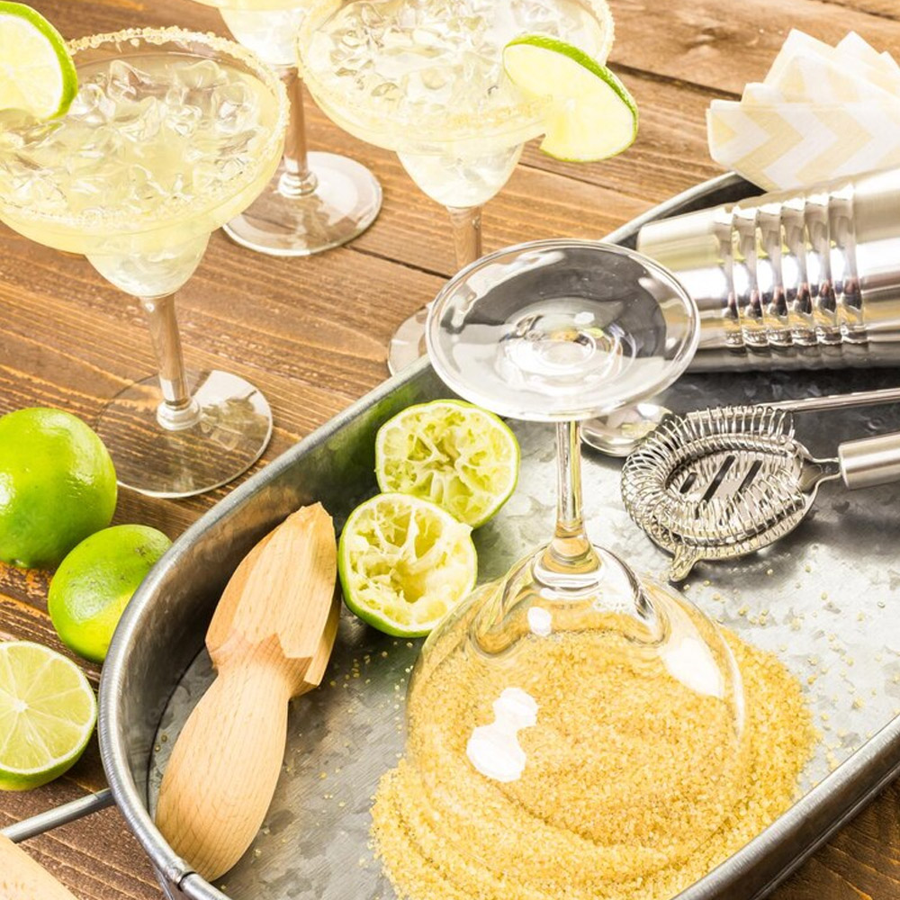 A serving tray with marggarita ingredients next to a couple of margaritas