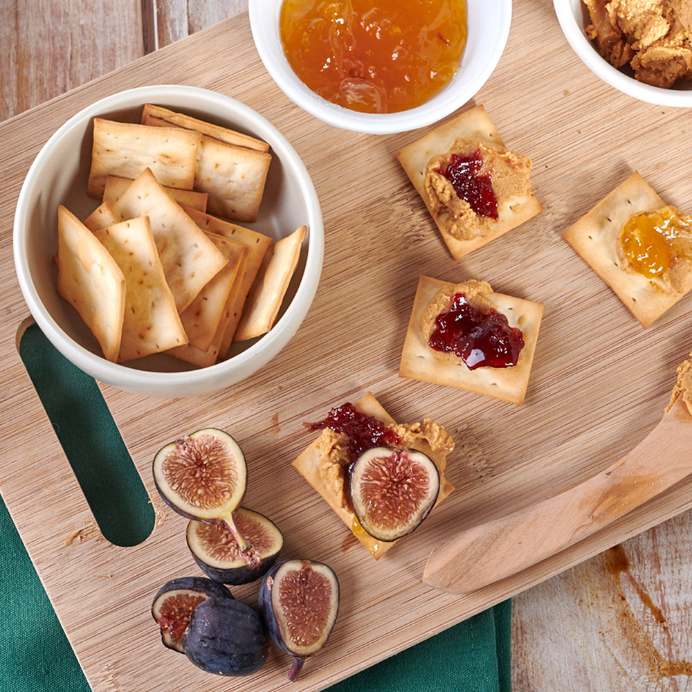 A bowl of crackers on a wood board with figs and crackers topped with toppings