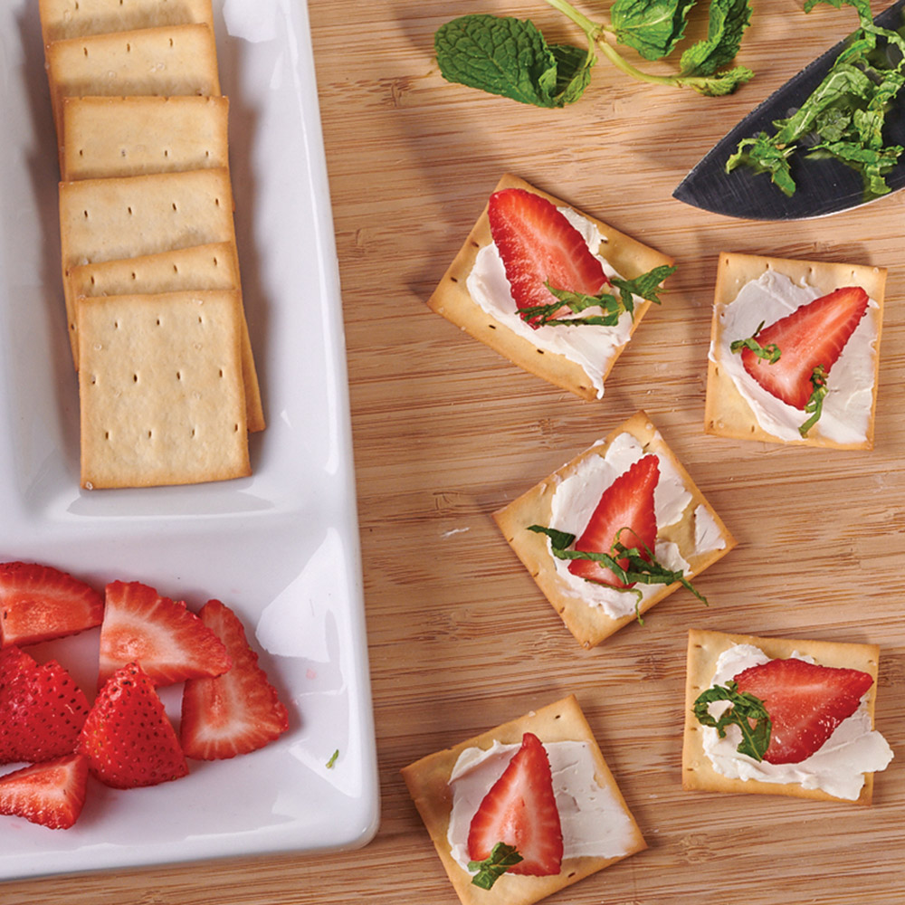 A plate with crackers and strawberries next to crackers topped with strawberries