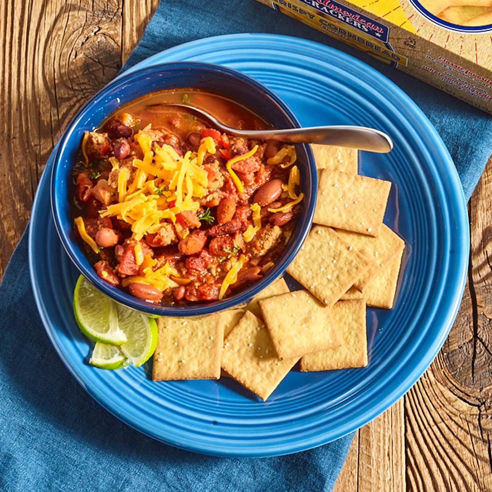 A bowl of chili on a plate with crackers