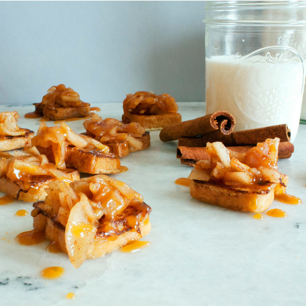 Mini toasts topped with apples and cinnamon next to a glass of milk
