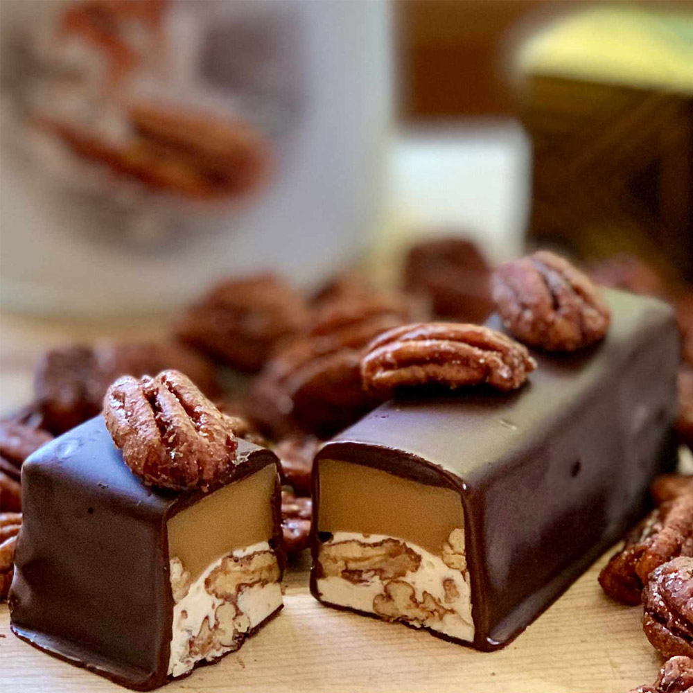 A Nutkrack Magic bar cut open on a wood surface surrounded by pecans