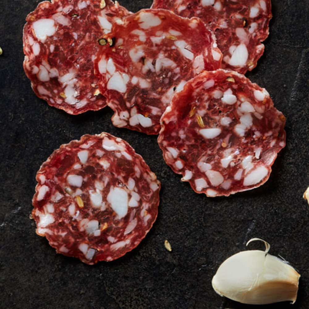 Slices of salami on a dark background next to a clove of garlic