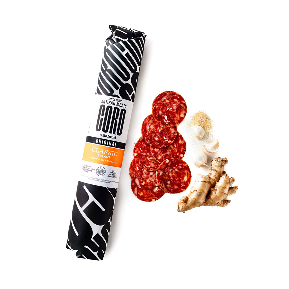 A wrapped stick of Coro Classic salami next to slices of salami