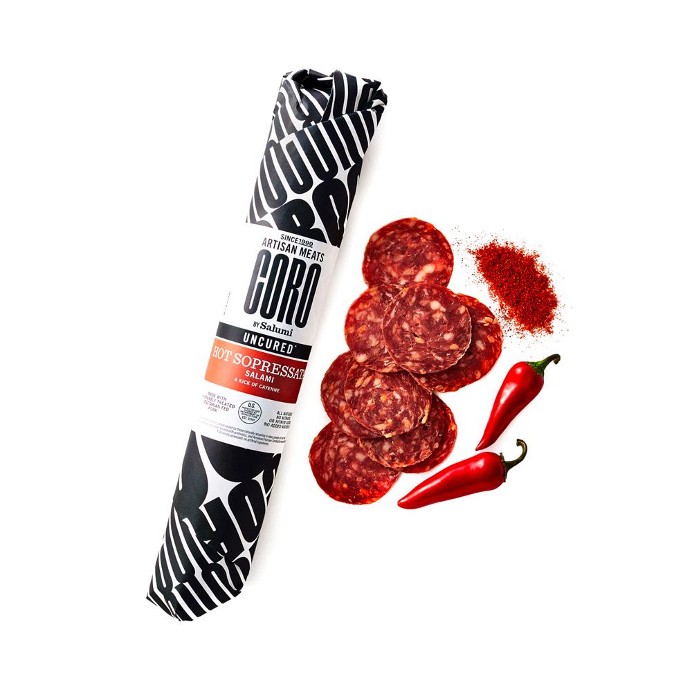 A wrapped stick of Coro Hot Sopressata salami next to slices of salami