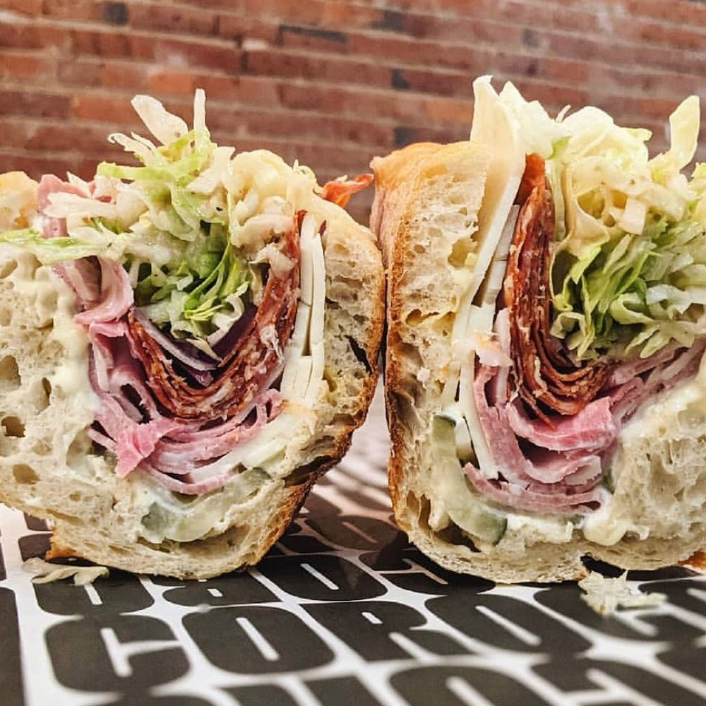 A close-up of a salami sub sandwich on a brick background