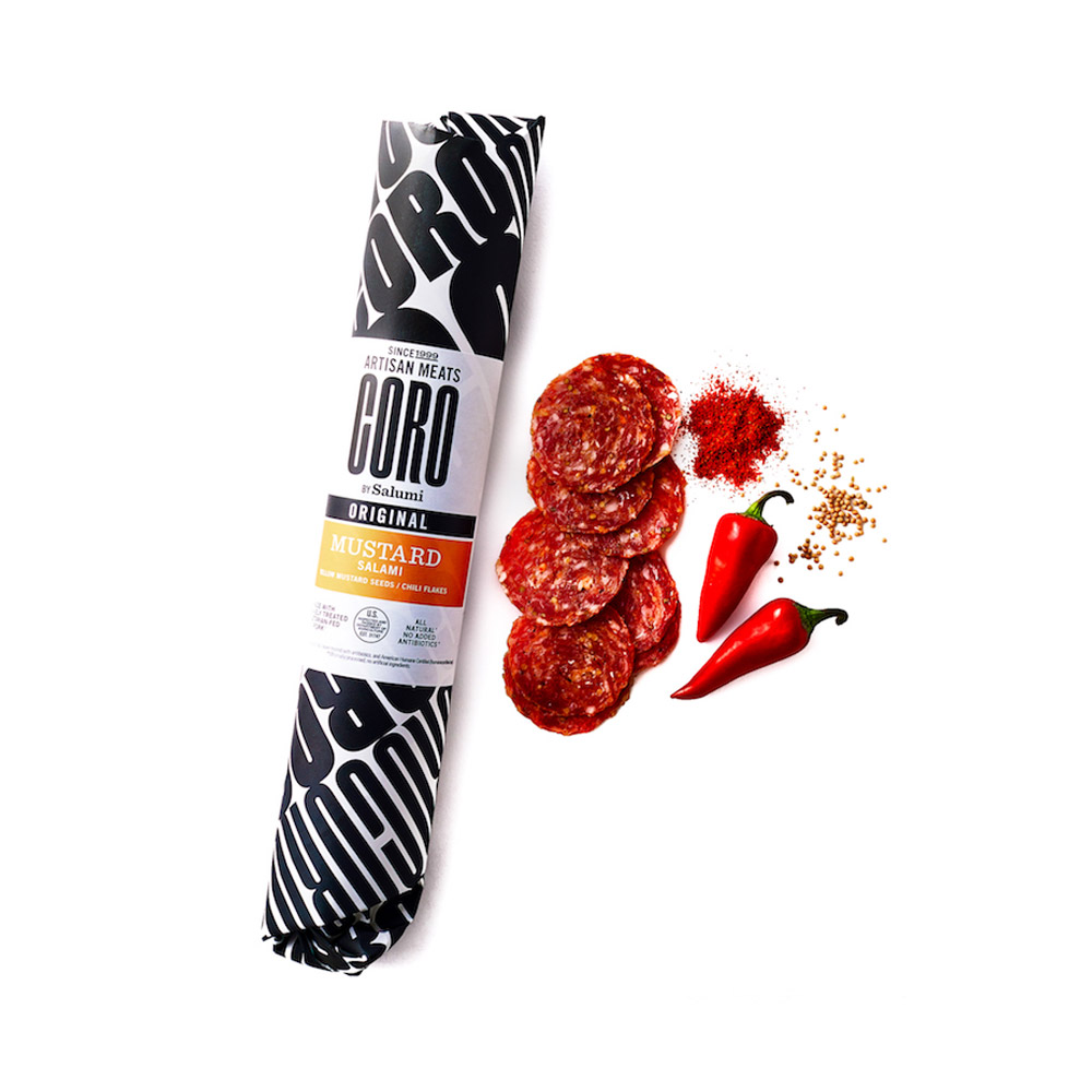 A wrapped stick of Coro Mustard salami next to slices of salami