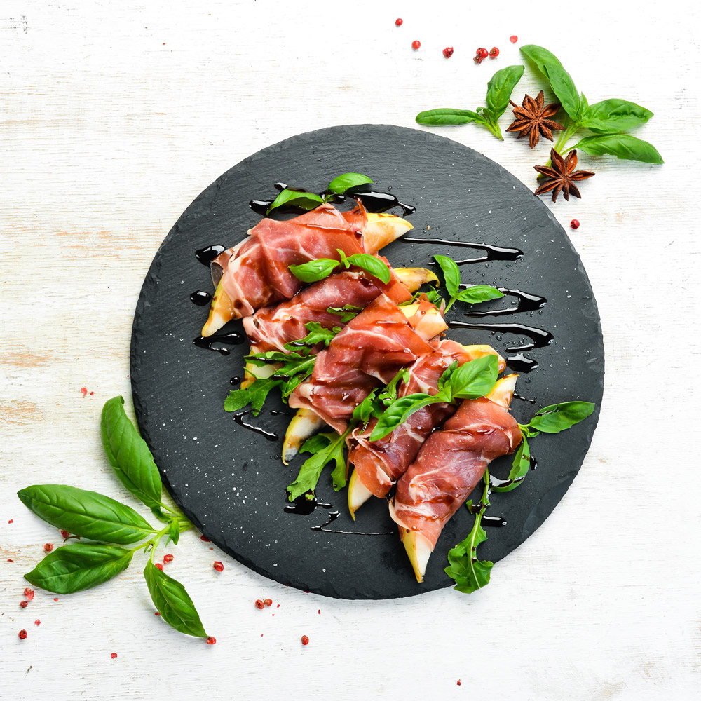 Prosciutto with pear and basil on a black stone plate