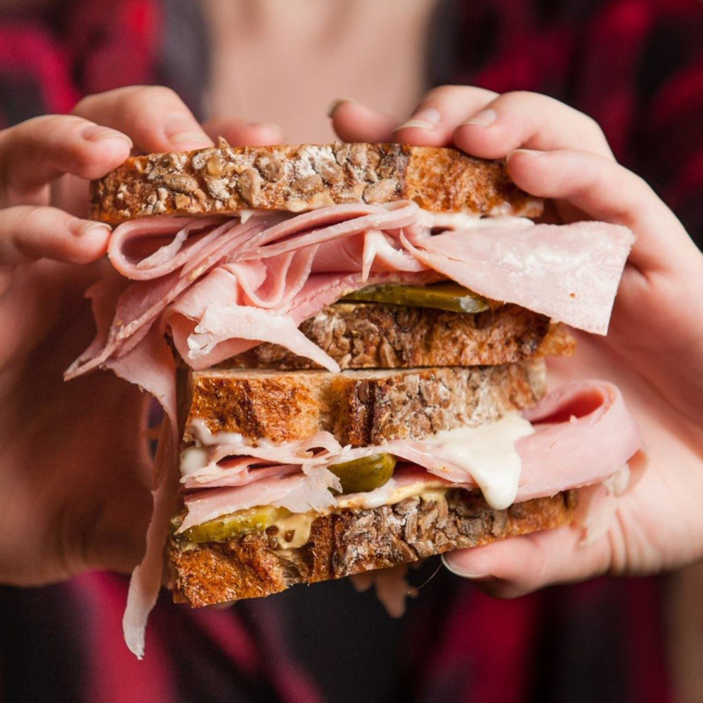 les trois petits cochons jambon de paris sliced on a sandwich being held by hands