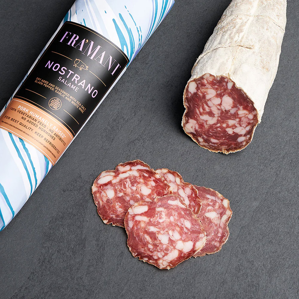 fra'mani salame nostrano in paper wrap next to slices of salami and an unwrapped salami chub