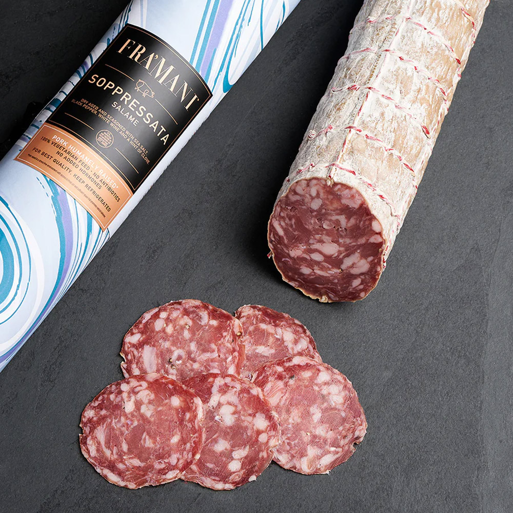 fra'mani sopressata in paper wrap next to slices of salami and an unwrapped salami chub