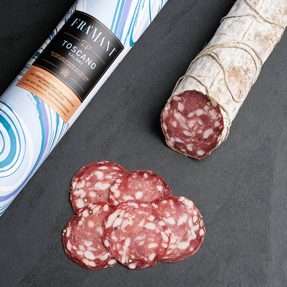 fra'mani salame toscano in paper wrap next to slices of salami and an unwrapped salami chub
