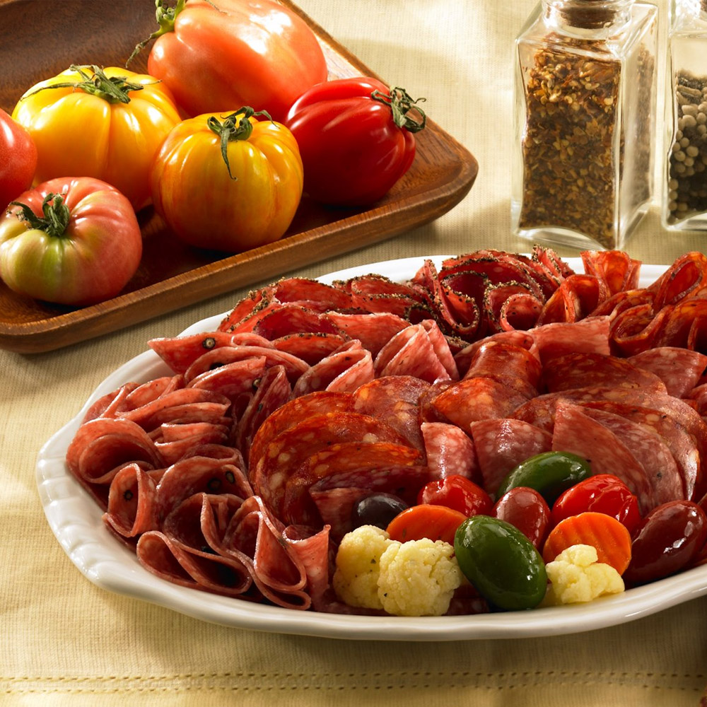 A salami platter next to a tray of tomatoes and some spice containers