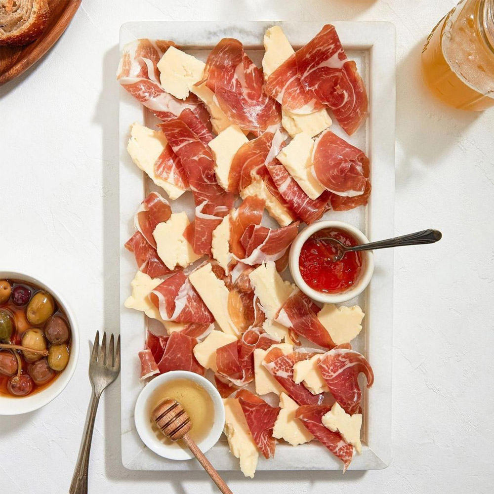 Prosciutto and cheese on a plate next to a bowl of olives and cocktails