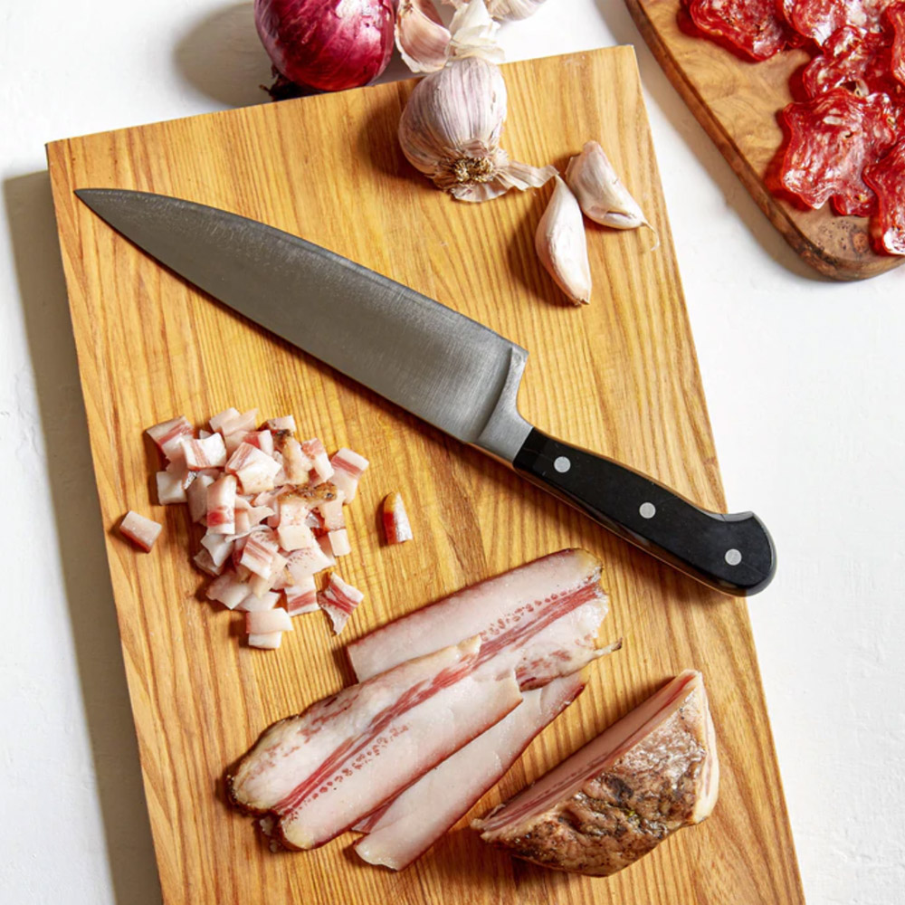 Slices of guianciale on a cutting board with a knife and some garlic