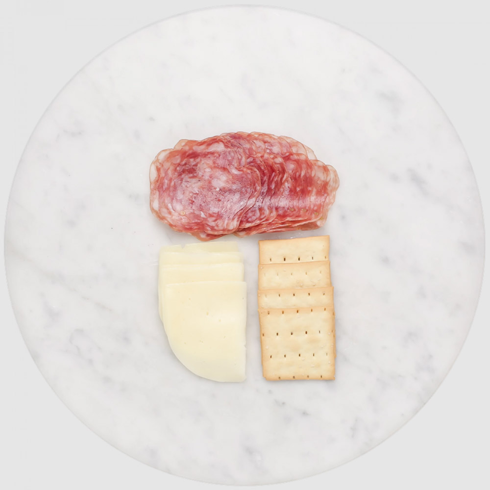 Slices of salami and cheese on a marble board with crackers