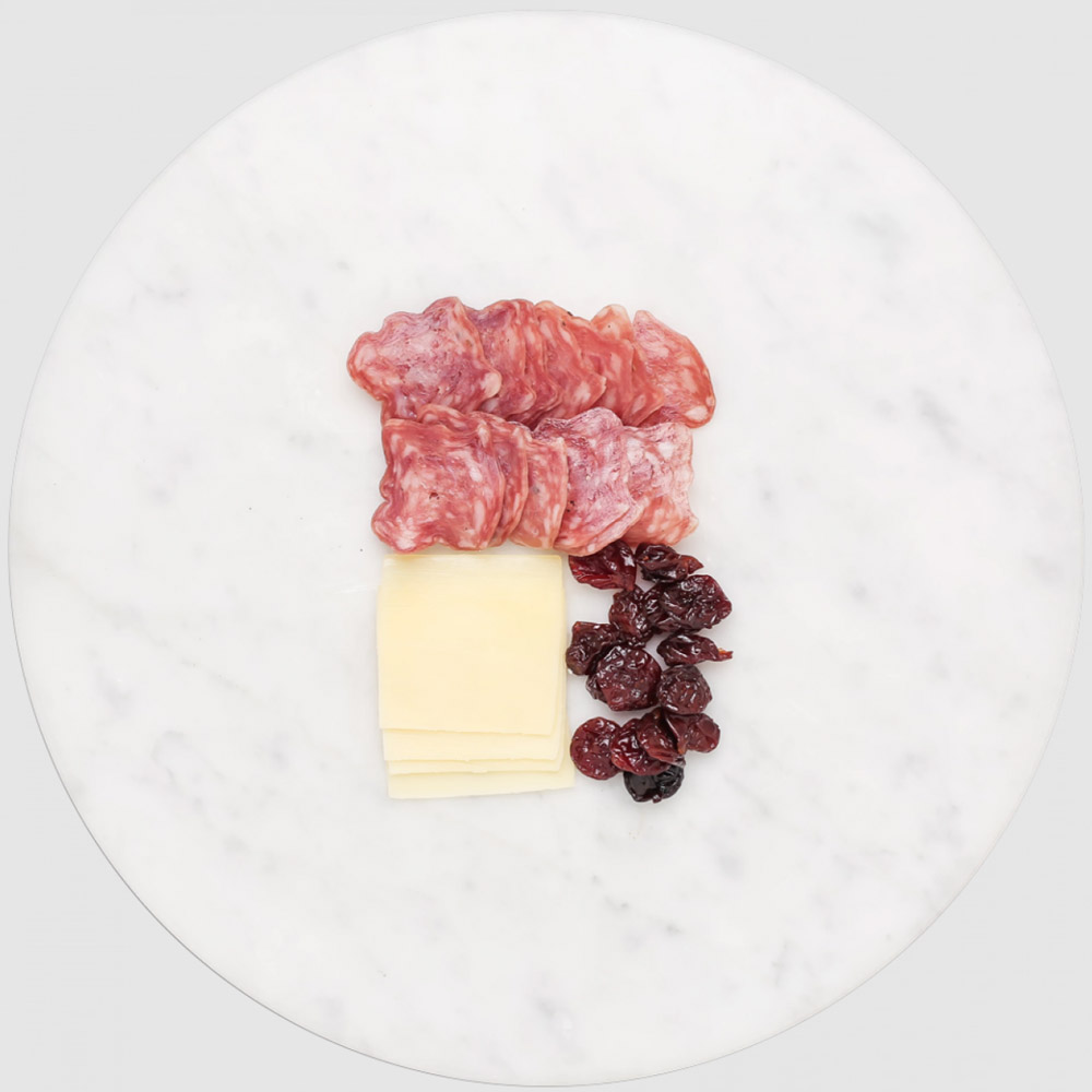 Sliced salami and cheese and dried cherries on a marble board