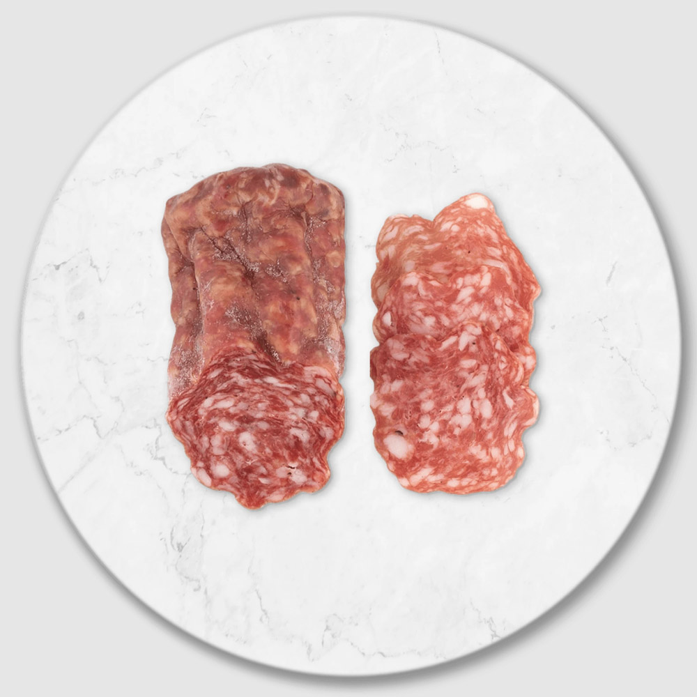 A portion of a salami stick next to slices of salami on a marble board
