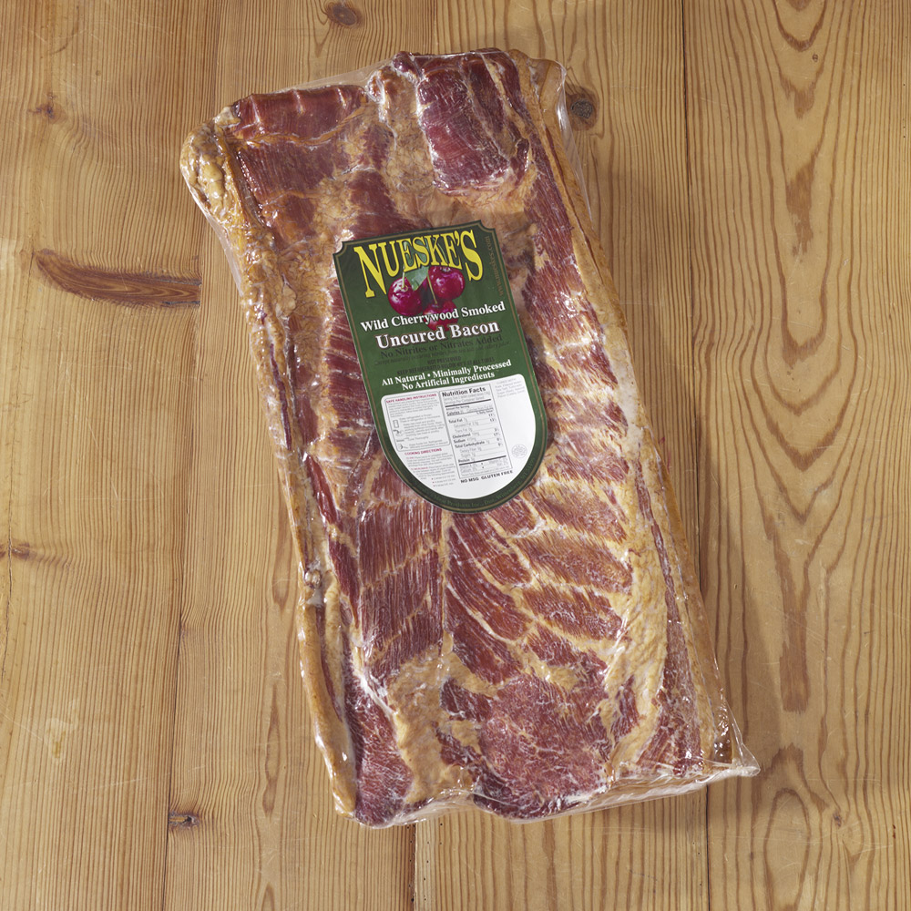nueske's wild cherrywood smoked uncured slab bacon in plastic packaging on wooden table