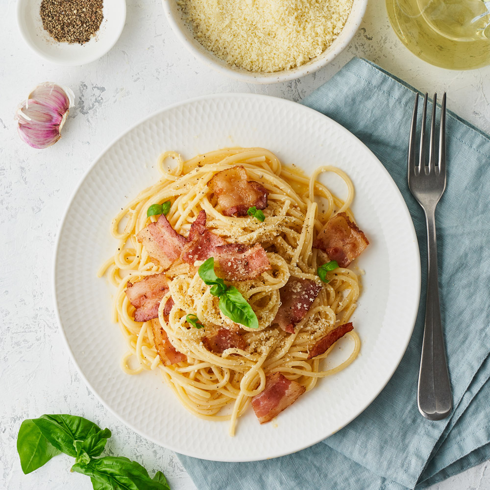 Pasta carbonara next to a fork and napkin and other ingredients