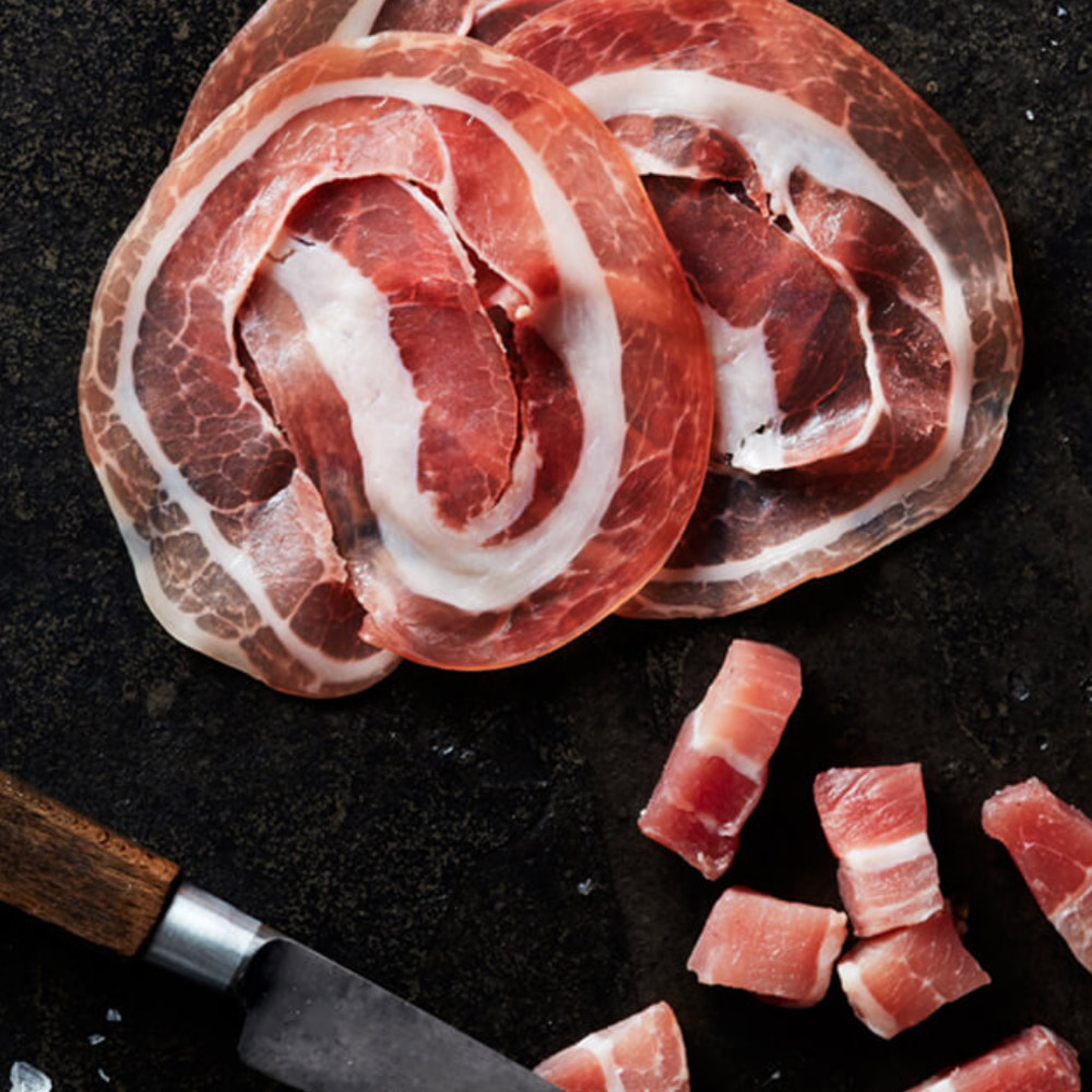 Slices and cubes of pancetta on a dark background