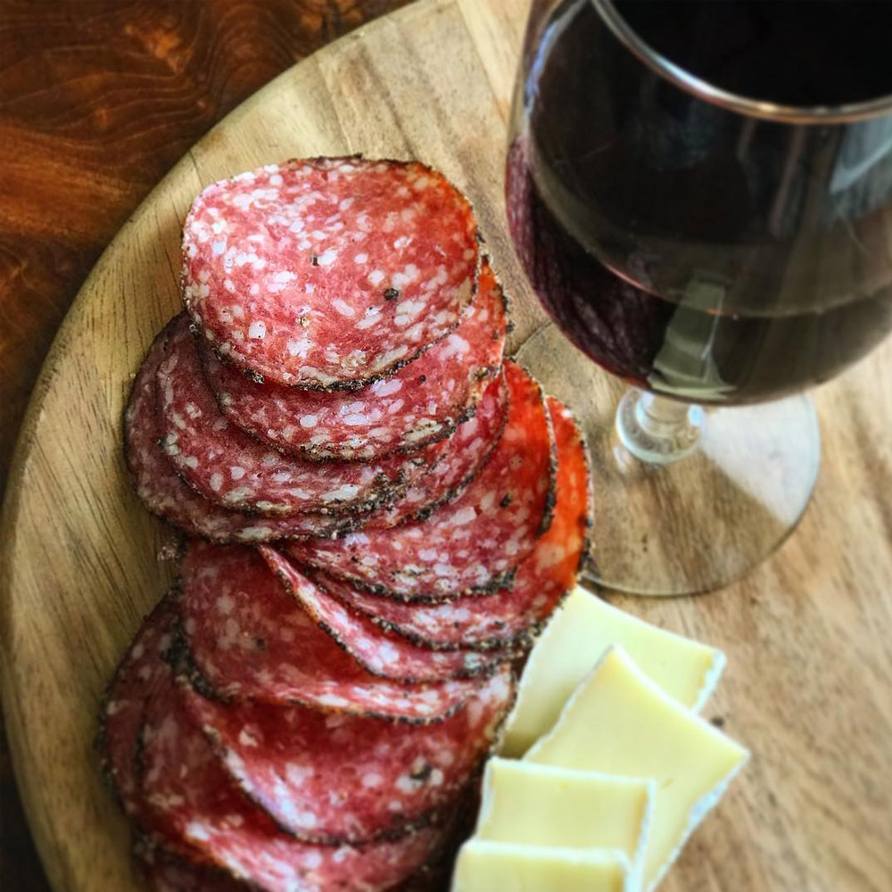 Slices of salami on a board next to a glass of wine and cheese