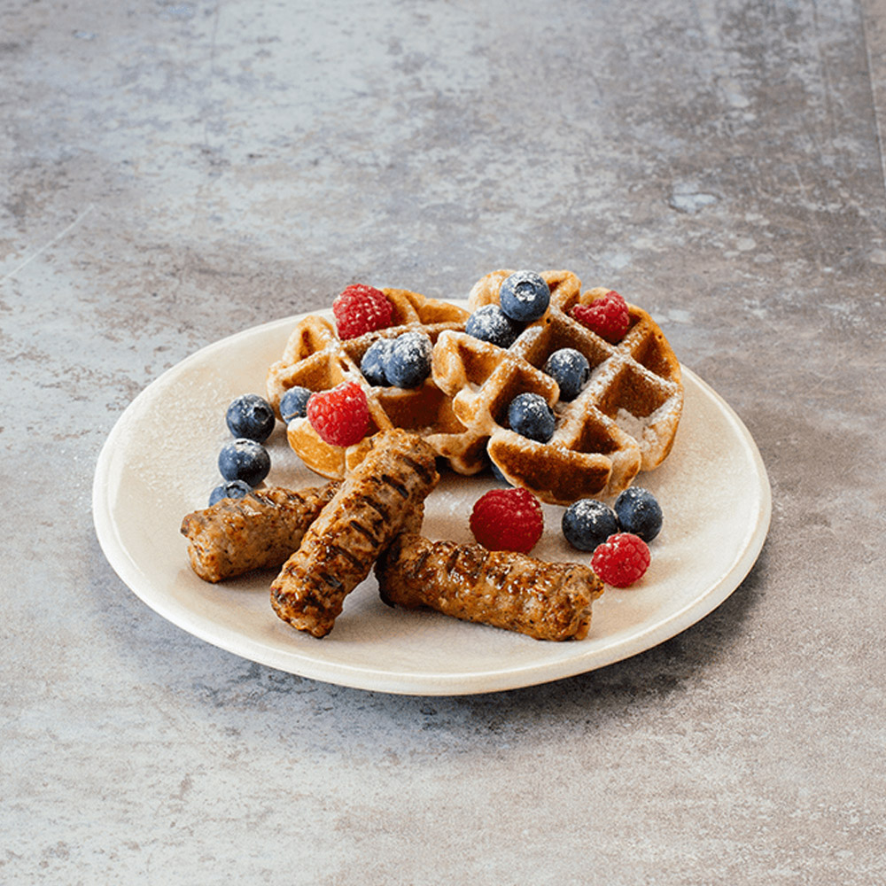 applegate naturals chicken & apple breakfast sausage links cooked on plate with waffles and blueberries and raspberries covered in powdered sugar