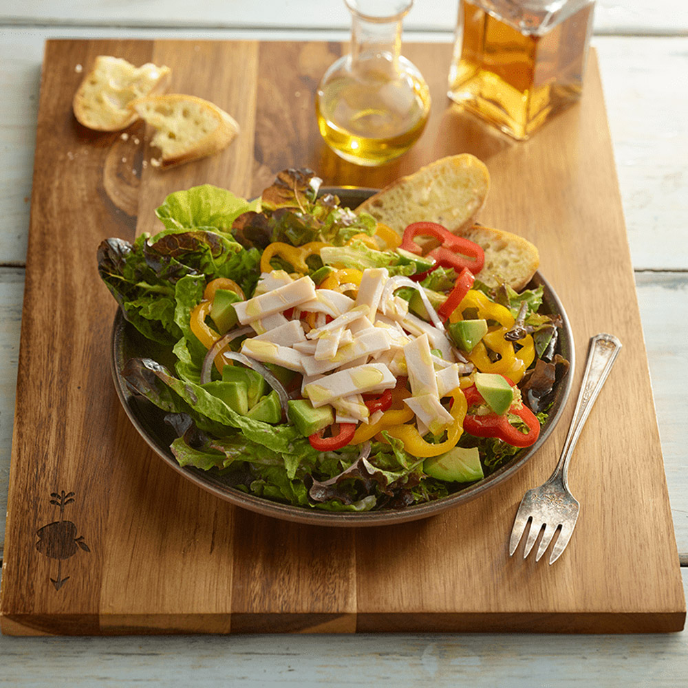 applegate organics sliced organic smoked chicken breast on salad with peppers and lettuce and onions and avocado on plate with bread on cutting board