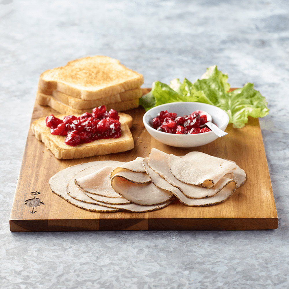 applegate naturals sliced herb turkey breast on salad with accompaniments on cutting board