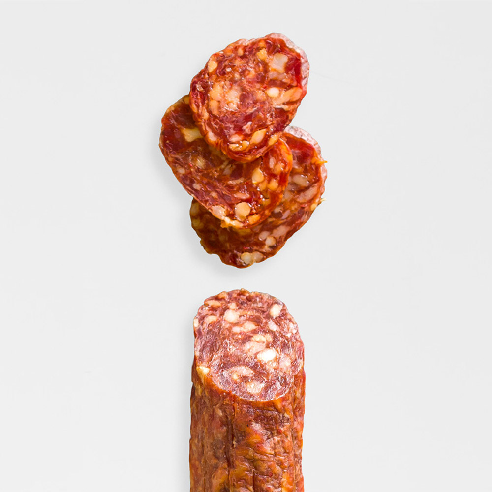 A Salami chub with slices of salami on a grey background