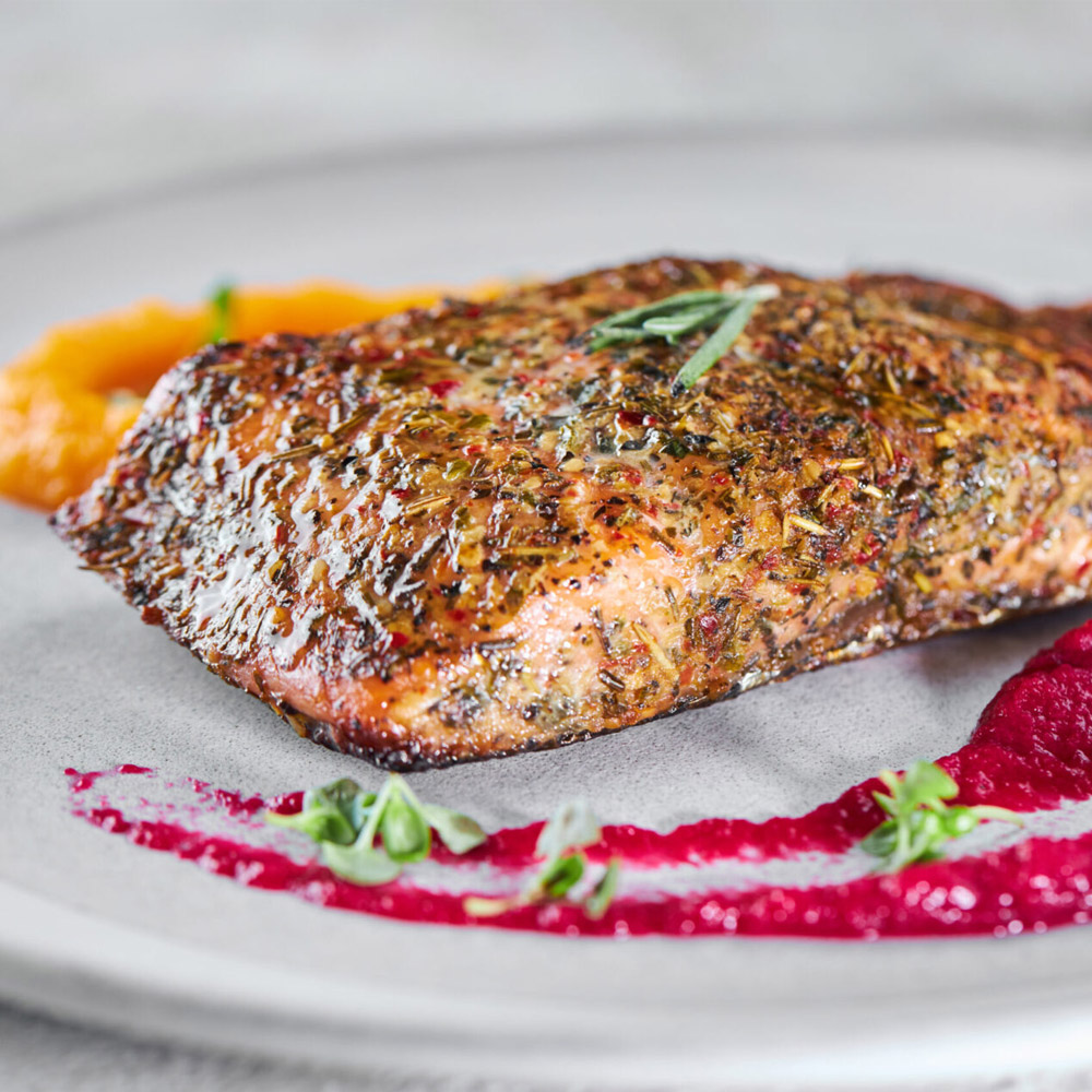 A salmon filet on a plate next to beet puree