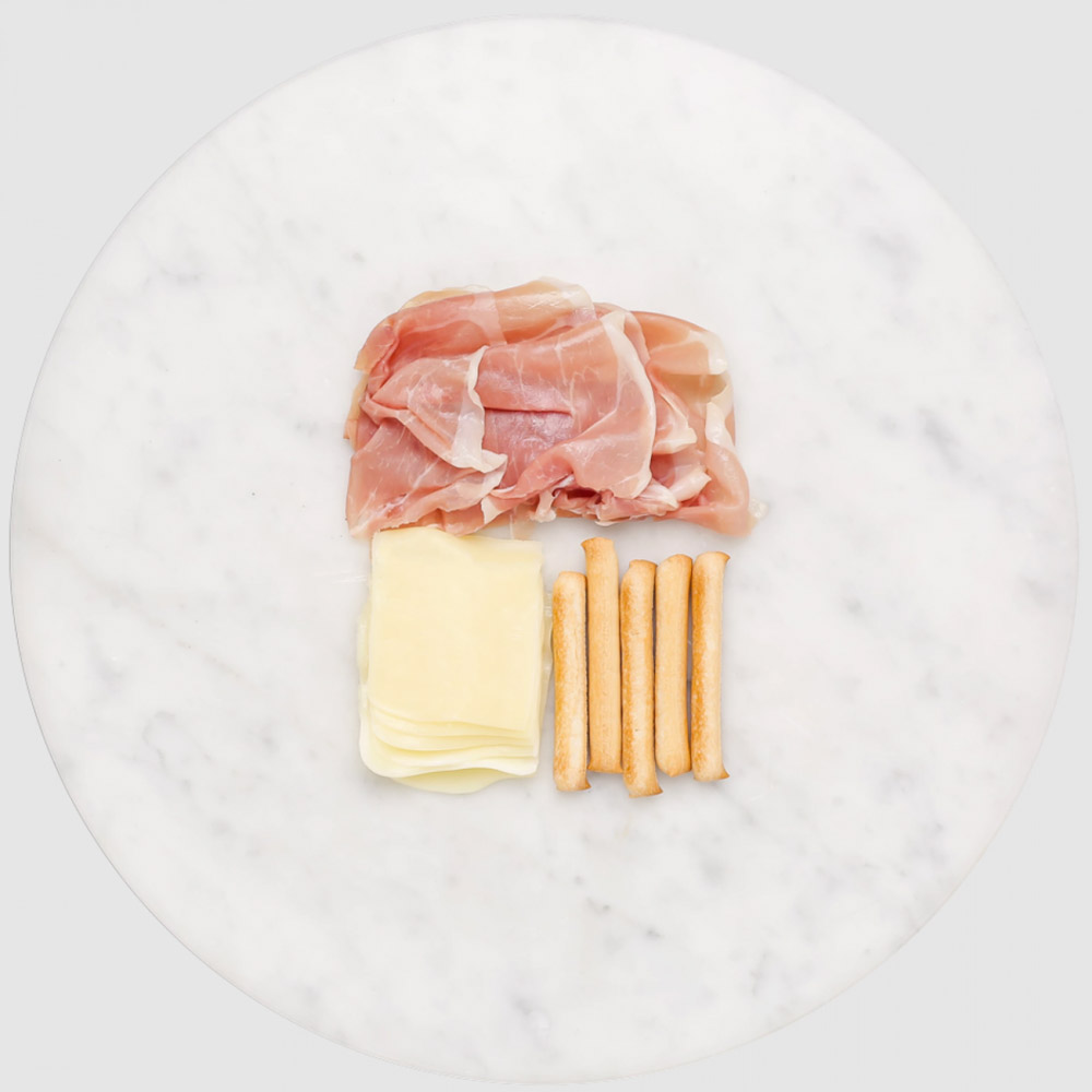 Slices of prosciutto and cheese on a marble board with breadsticks