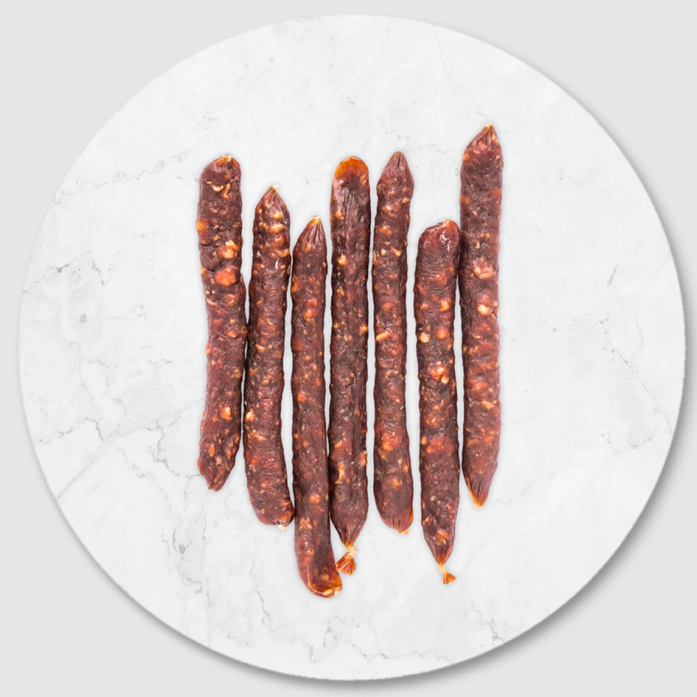 Seven thin mini salami sticks on a marble board