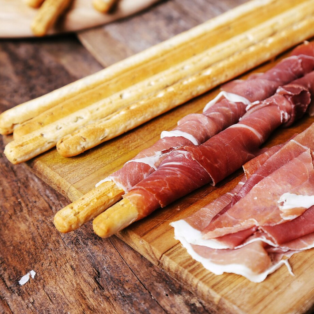 Slices of prosciutto wrapped around breadsticks on a wood board