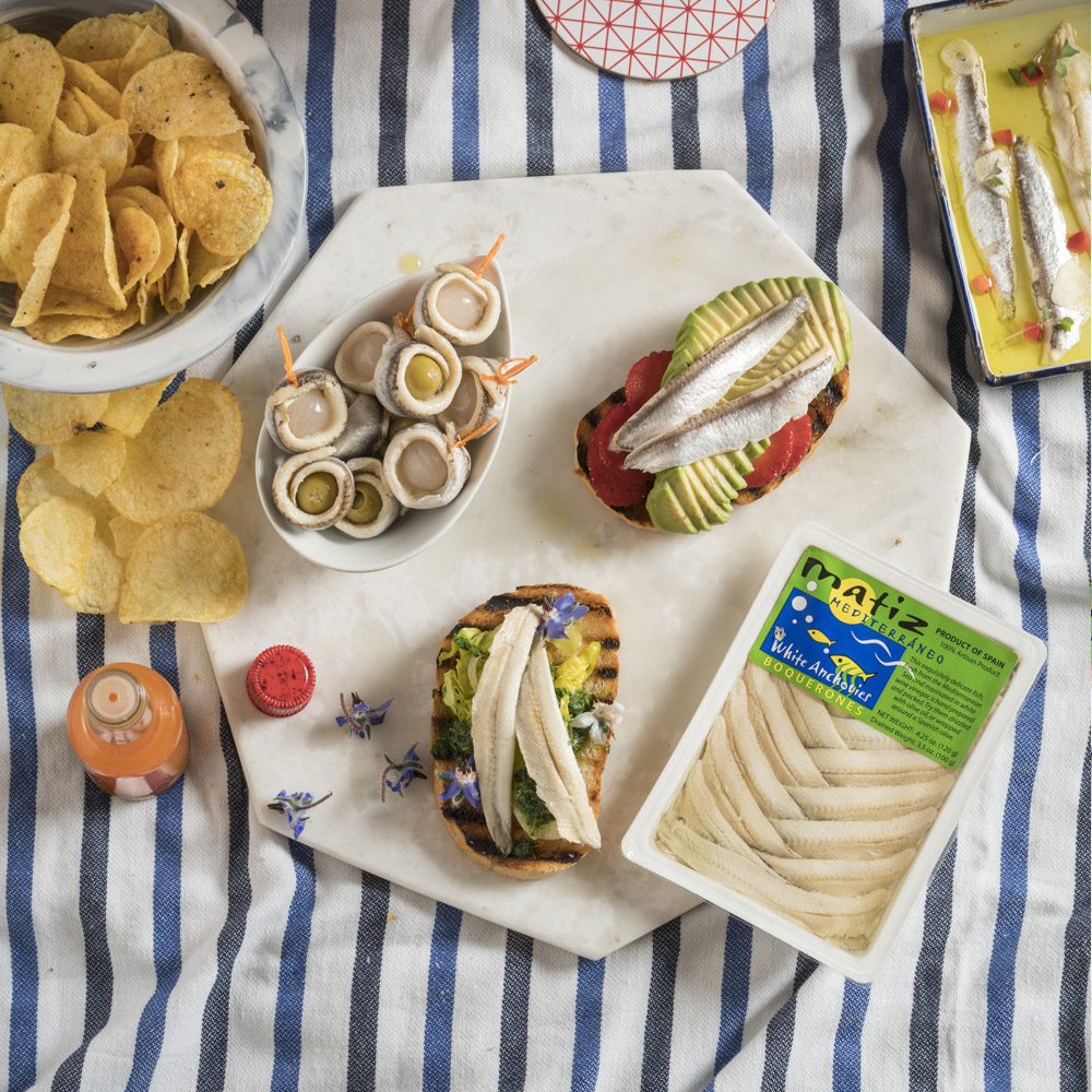 Matiz anchovies on a picnic blanket surrounded by other snacks