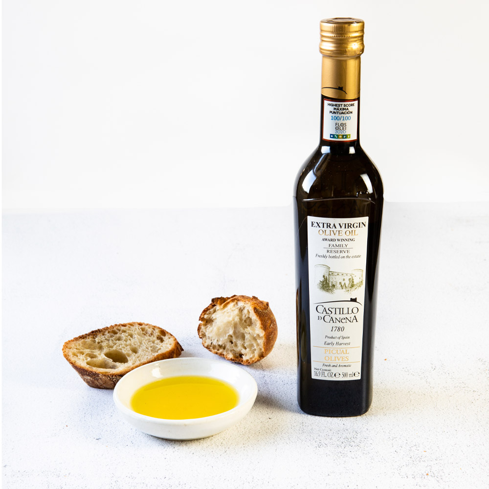 bottle of castillo de canena picual family reserve extra virgin olive oil with oil in cup and bread