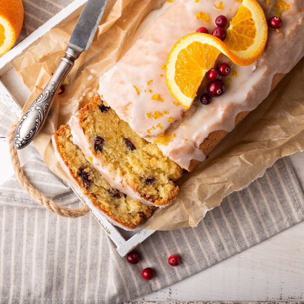Orange cake with cranberries and sugar icing on white rustic wooden background